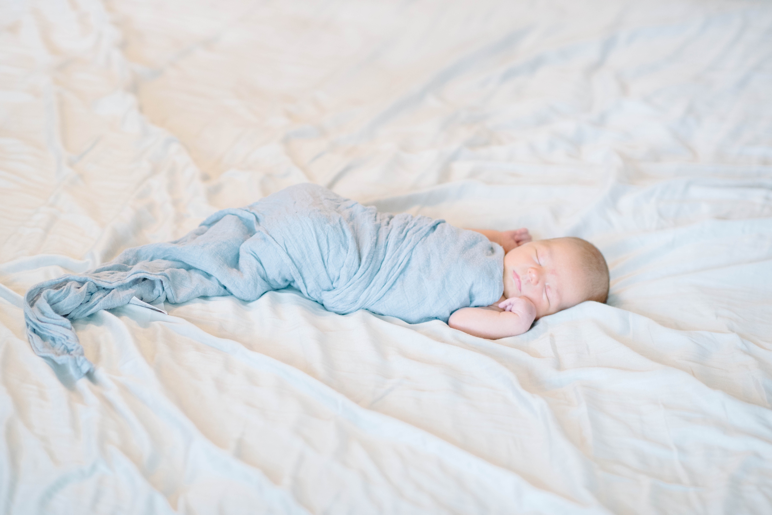 newborn baby in blue swaddle sleeping on white bed