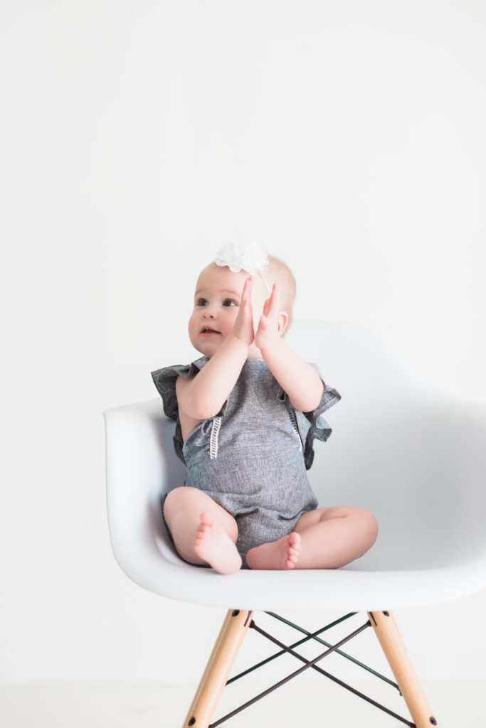 baby girl in grey romper with white bow clapping