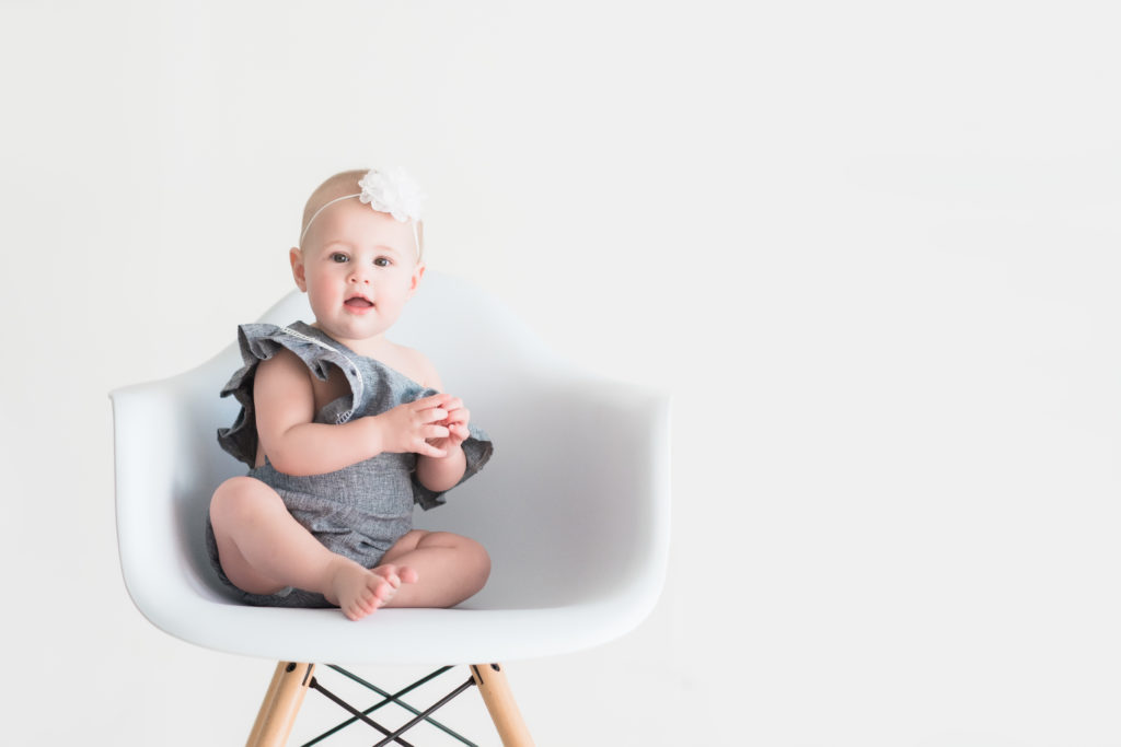 baby girl with white bow on white modern chair