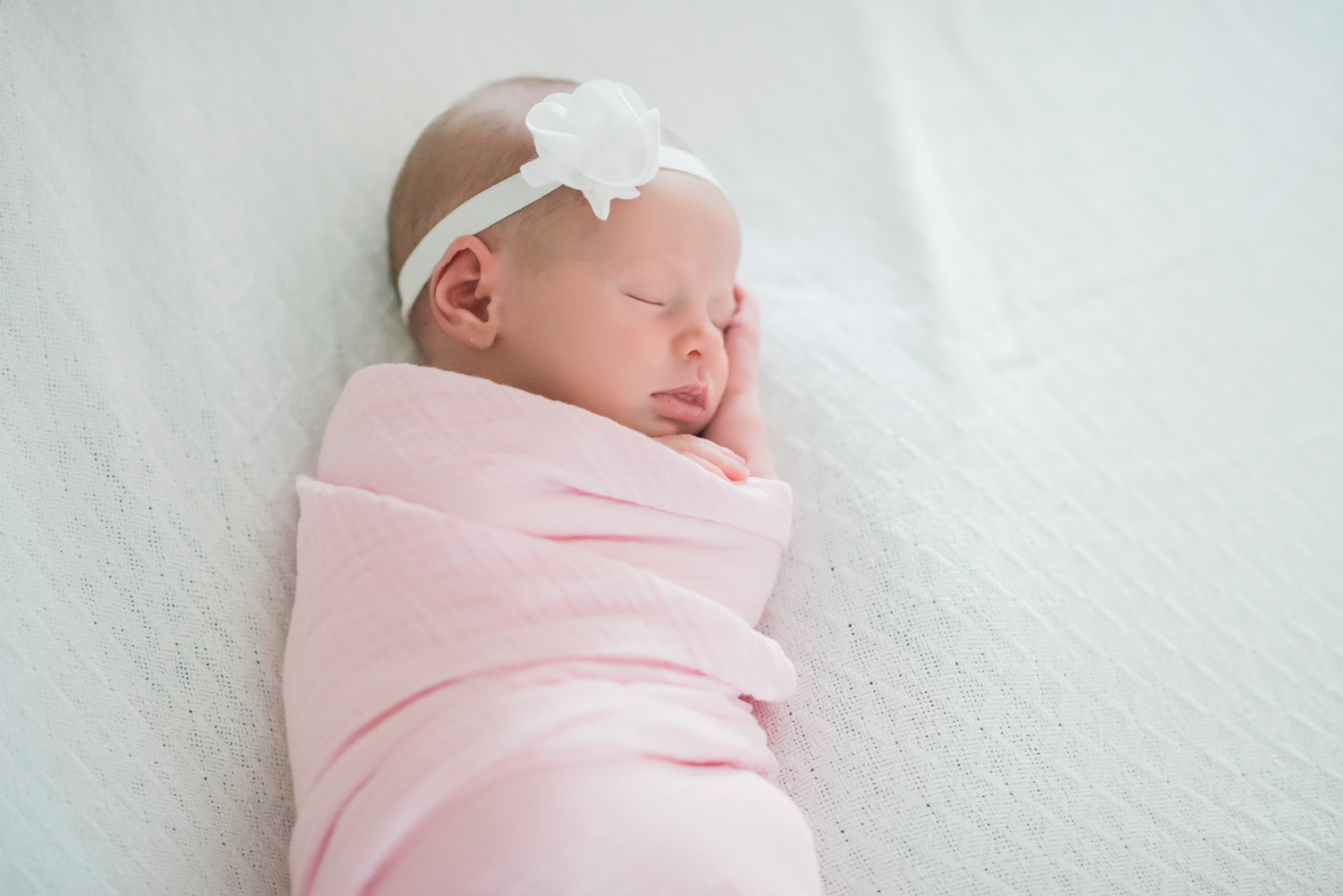 baby girl sleeping wrapped in pink blanket on white sheet