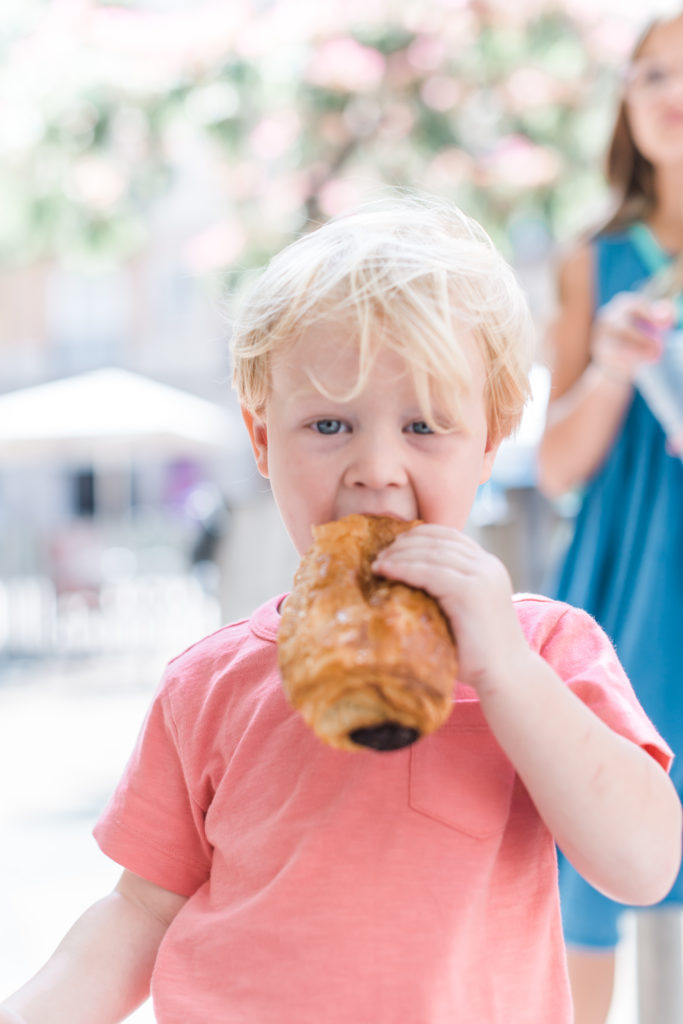  two year old in orange shirt eating chocolate croissant 